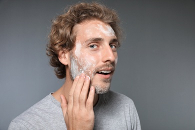 Young man washing face with soap on grey background