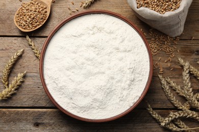 Wheat flour in bowl, spikes and grains on wooden table, flat lay