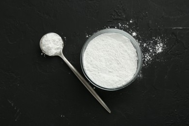 Photo of Baking powder in bowl and spoon on black textured table, top view