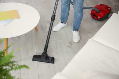 Young man using vacuum cleaner at home, closeup