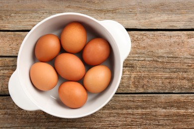 Photo of Unpeeled boiled eggs in saucepan on old wooden table, top view. Space for text