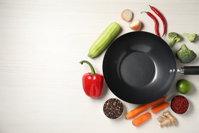 Empty iron wok surrounded by raw ingredients on white wooden table, flat lay. Space for text