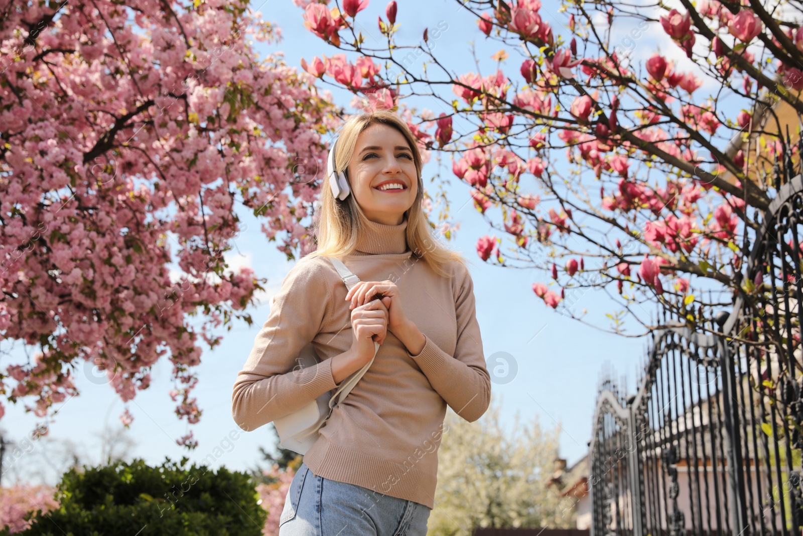 Photo of Happy woman with headphones listening to audiobook outdoors on spring day