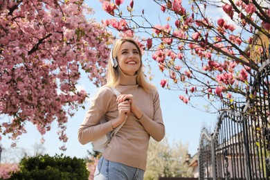 Happy woman with headphones listening to audiobook outdoors on spring day