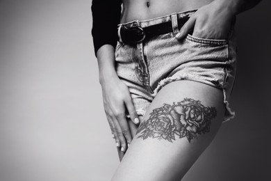Image of Beautiful woman with tattoo on leg against light background, closeup. Black and white photography