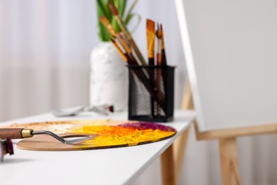 Art supplies on table near wooden easel with canvas indoors, closeup. Space for text