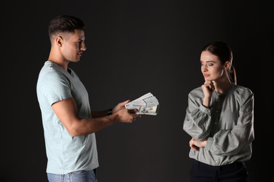 Man offering bribe to woman on black background