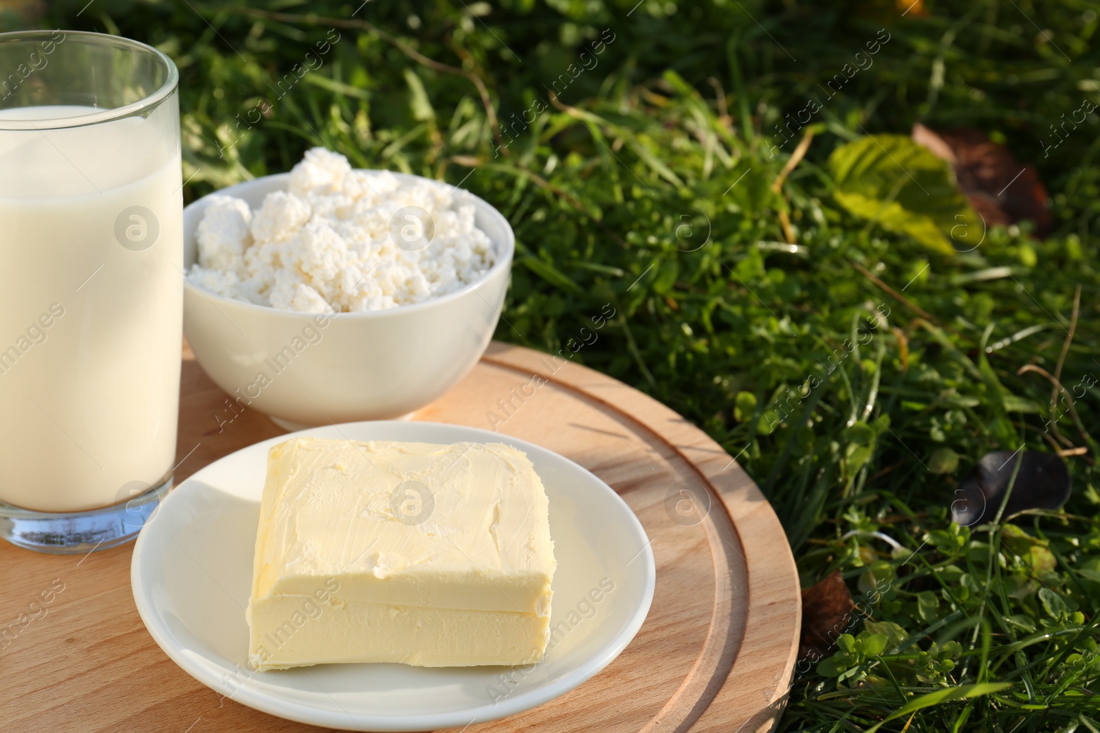 Photo of Wooden tray with tasty homemade butter and dairy products on grass outdoors, closeup. Space for text