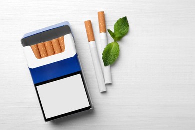 Photo of Menthol cigarettes, pack and mint on white wooden table, flat lay. Space for text