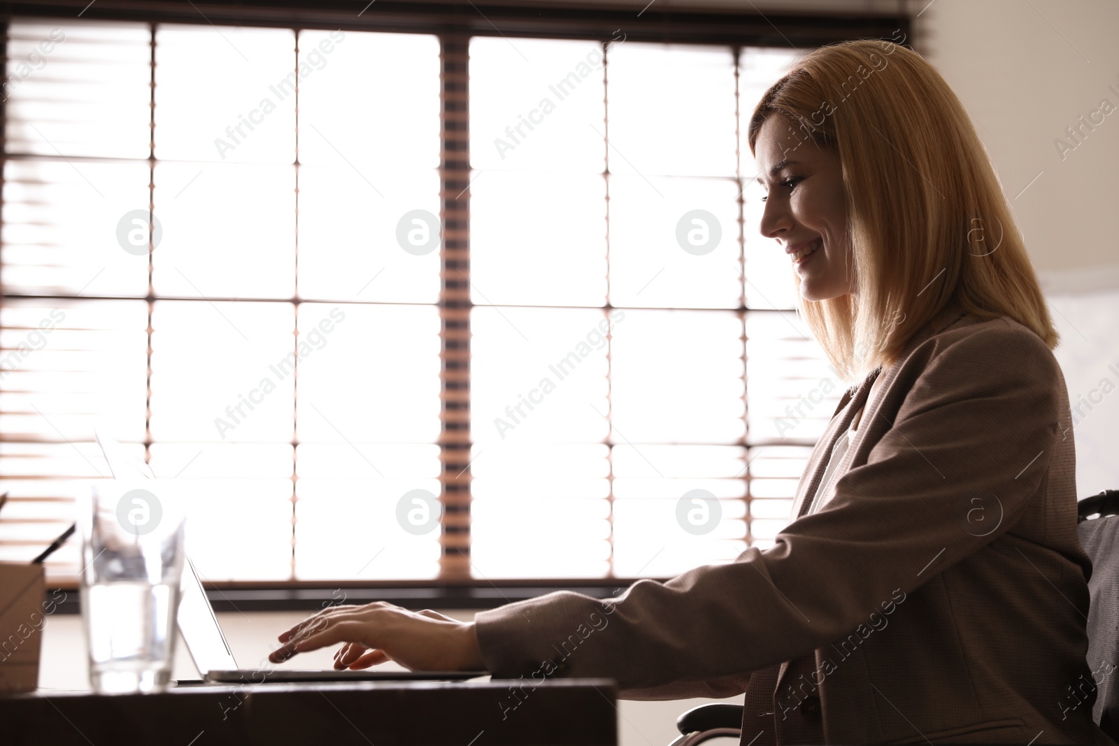 Photo of Woman in wheelchair working with laptop at table indoors