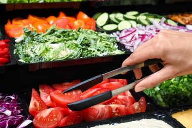 Young woman taking fresh tomatoes from salad bar, closeup