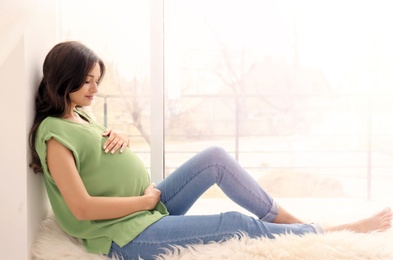 Beautiful pregnant woman sitting near window at home