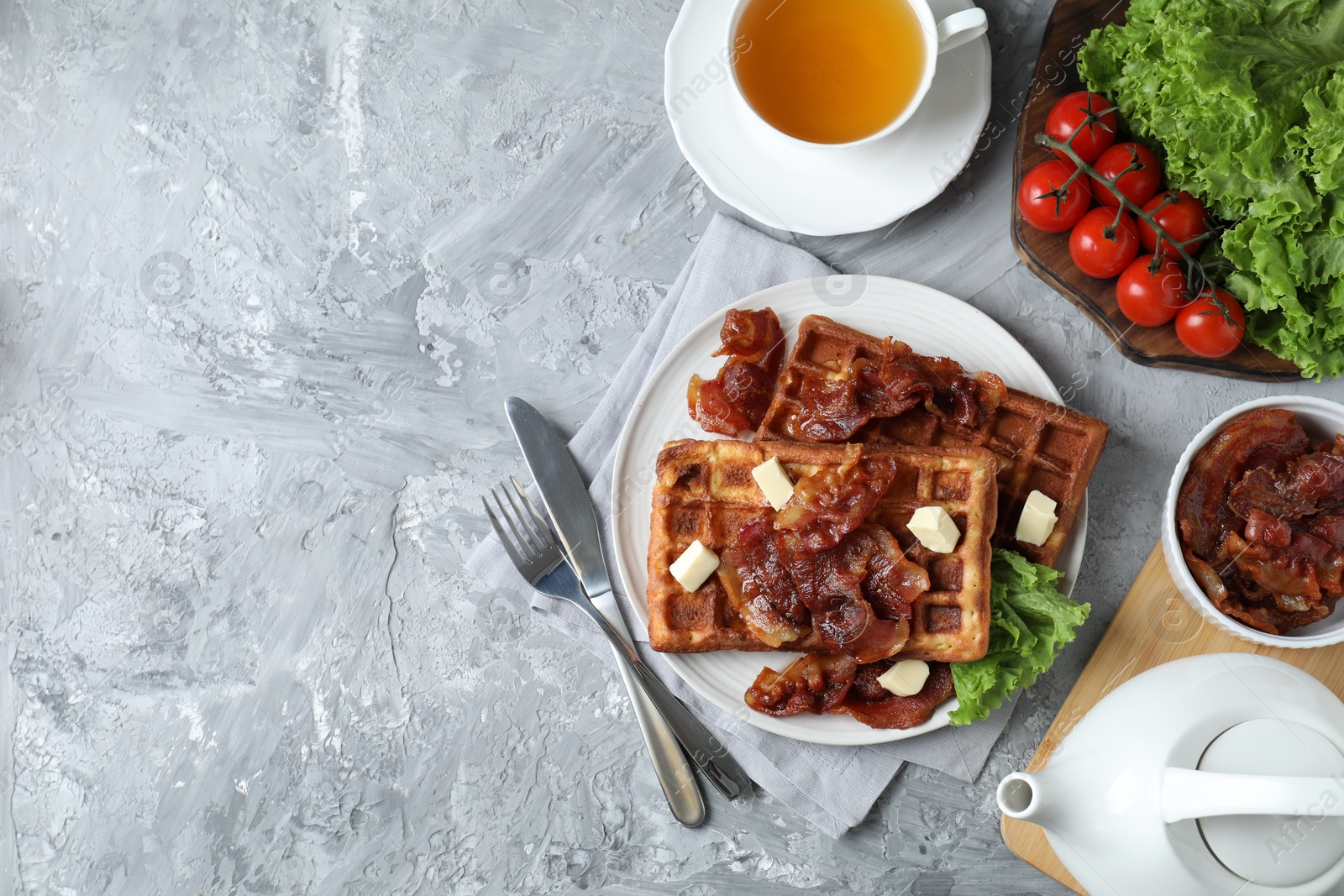 Photo of Delicious Belgium waffles served with fried bacon and butter on grey table, flat lay. Space for text