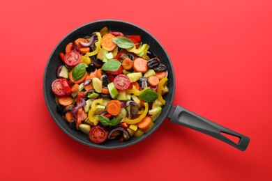 Photo of Mix of tasty vegetables in pan on red background, top view
