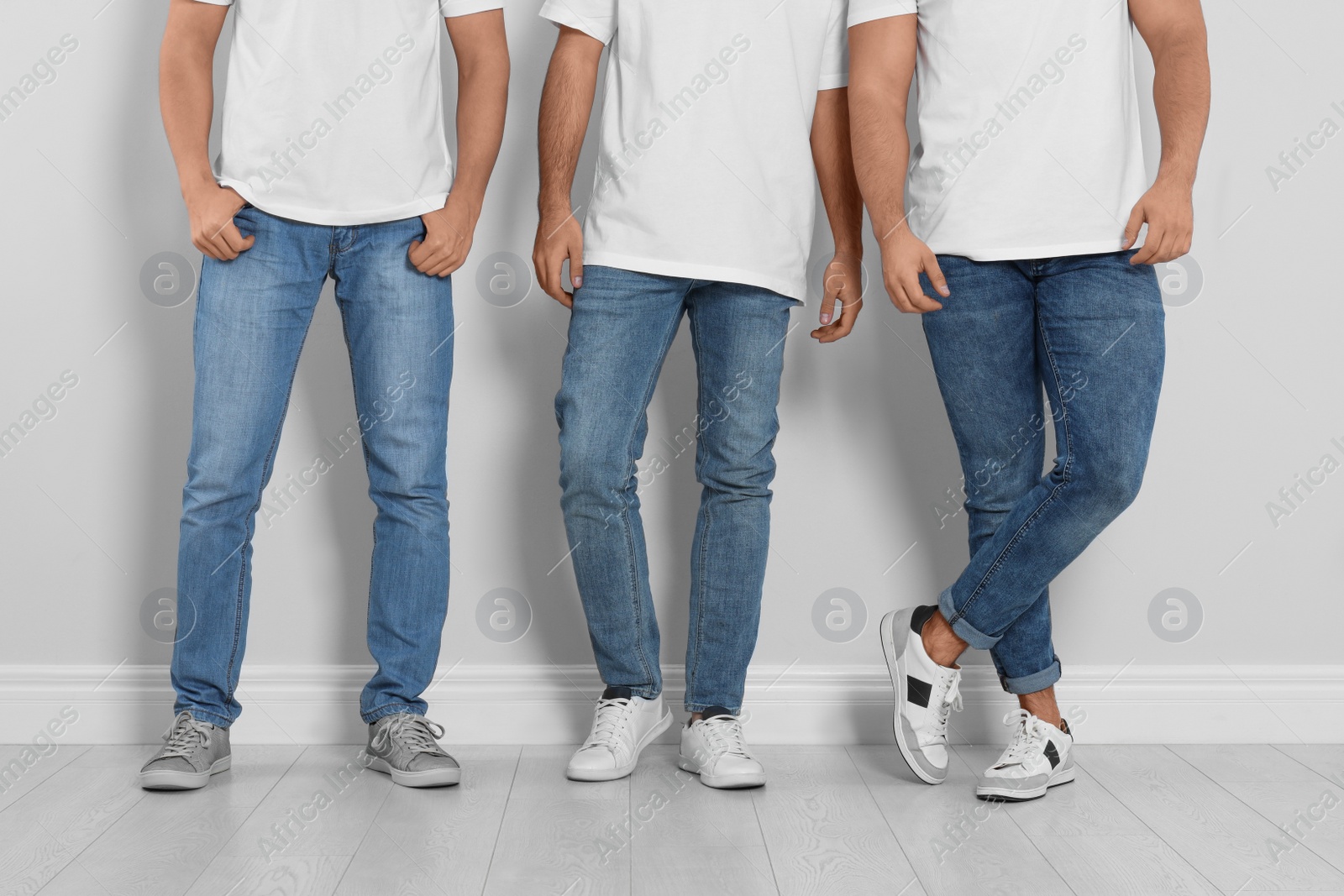 Photo of Group of young men in stylish jeans near light wall, closeup