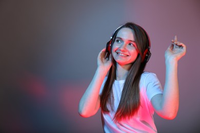 Portrait of beautiful woman with headphones on color background, space for text