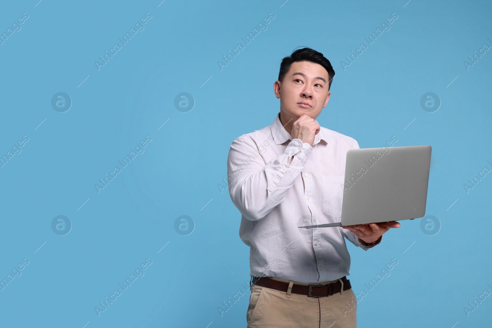 Photo of Thoughtful man with laptop on light blue background, space for text