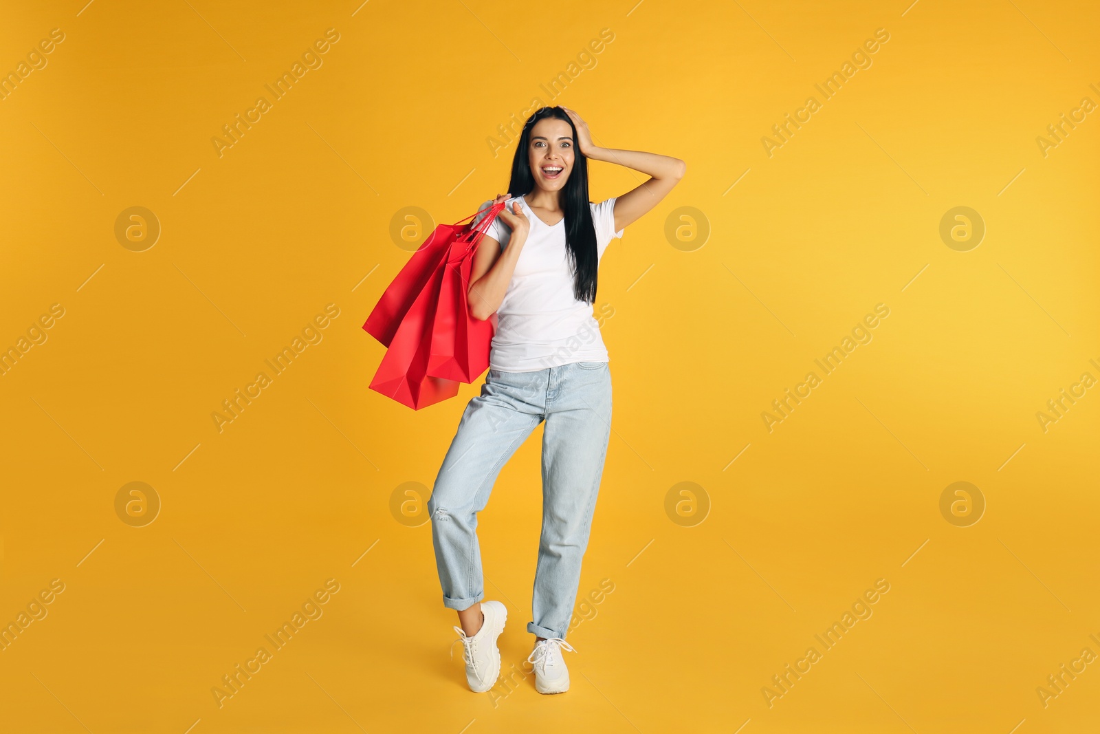 Photo of Beautiful young woman with paper shopping bags on yellow background