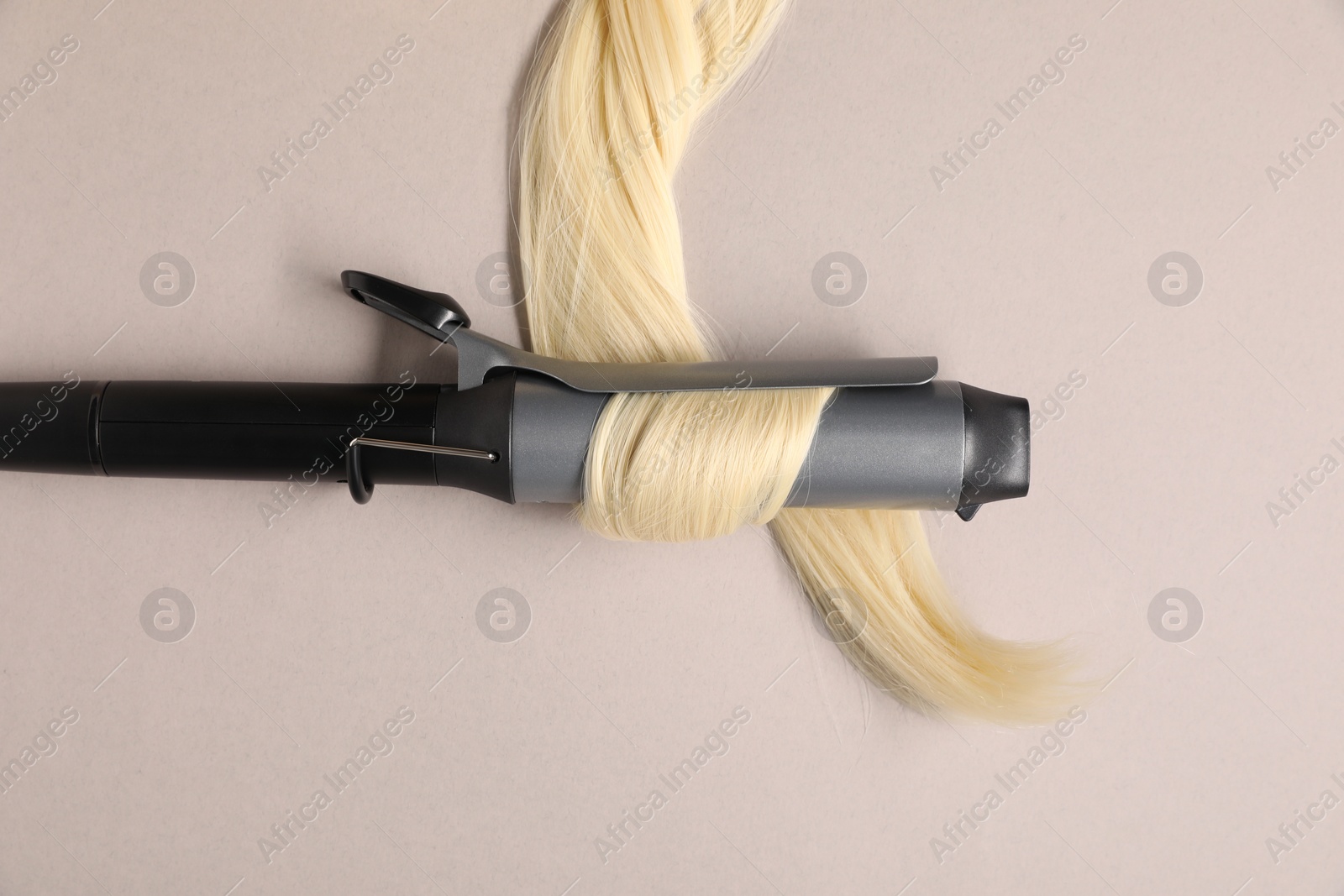 Photo of Curling iron with blonde hair lock on beige background, top view