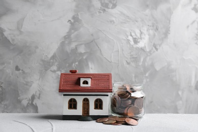 Photo of House model and jar with coins on table against grey background. Space for text