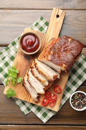 Photo of Pieces of baked pork belly served with sauce, chili pepper and parsley on wooden table, top view