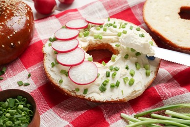 Photo of Delicious bagel with cream cheese, green onion and radish on table, closeup