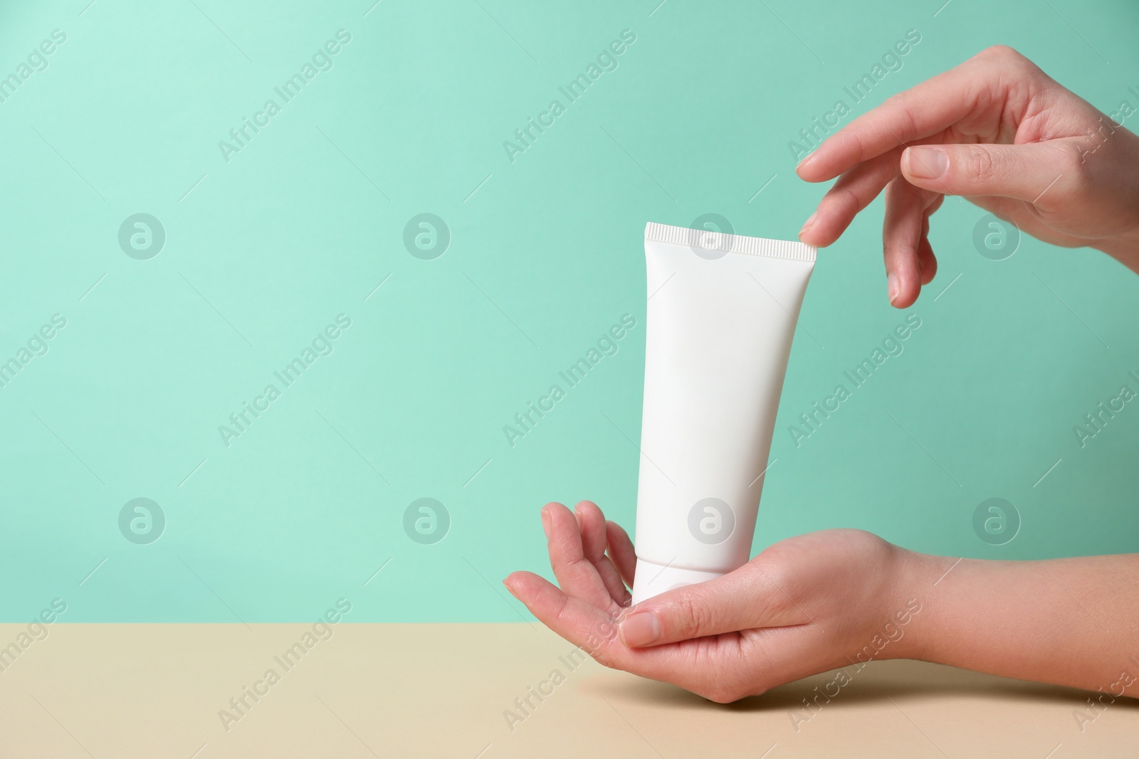 Photo of Tube of hand cream on beige table against turquoise background, closeup. Space for text