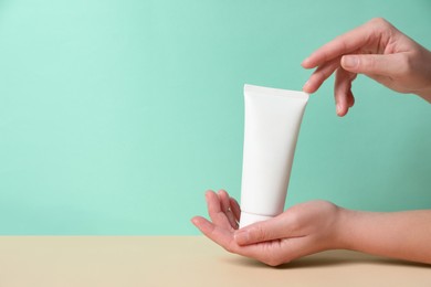 Photo of Tube of hand cream on beige table against turquoise background, closeup. Space for text