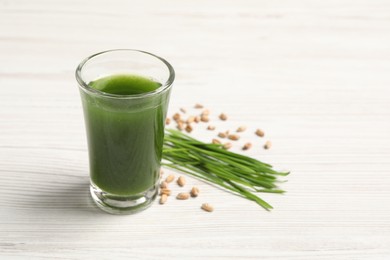 Photo of Wheat grass drink in shot glass, seeds and fresh green sprouts on white wooden table, closeup