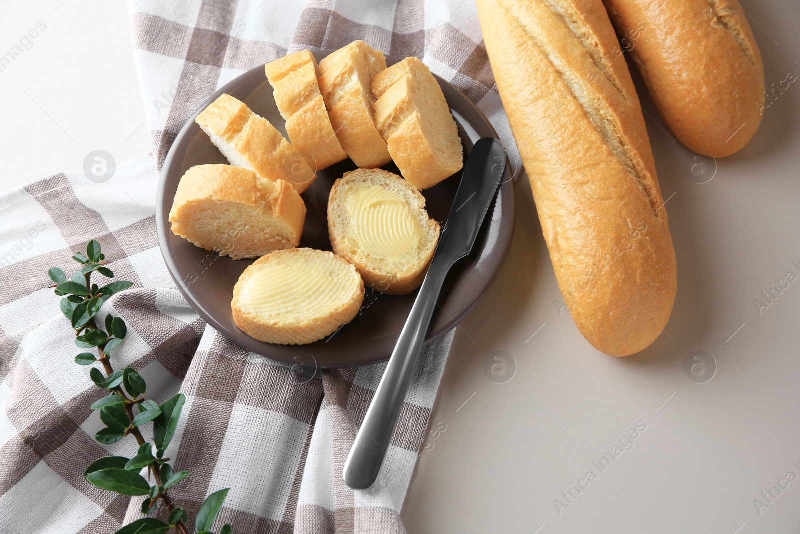 Photo of Whole and cut baguettes with fresh butter on table, above view