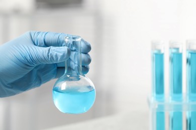 Photo of Scientist holding flask of light blue liquid in laboratory, closeup. Space for text