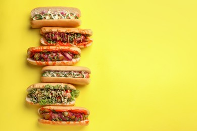 Photo of Delicious hot dogs with different toppings on yellow background, flat lay. Space for text