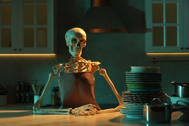 Photo of Human skeleton sitting at white marble table with clean dishware in kitchen at night