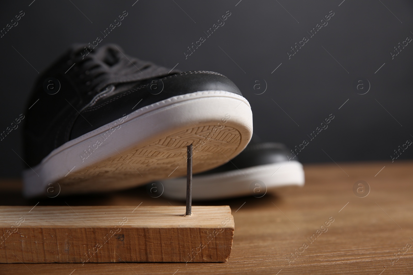 Photo of Metal nail in wooden plank and shoes on table, closeup