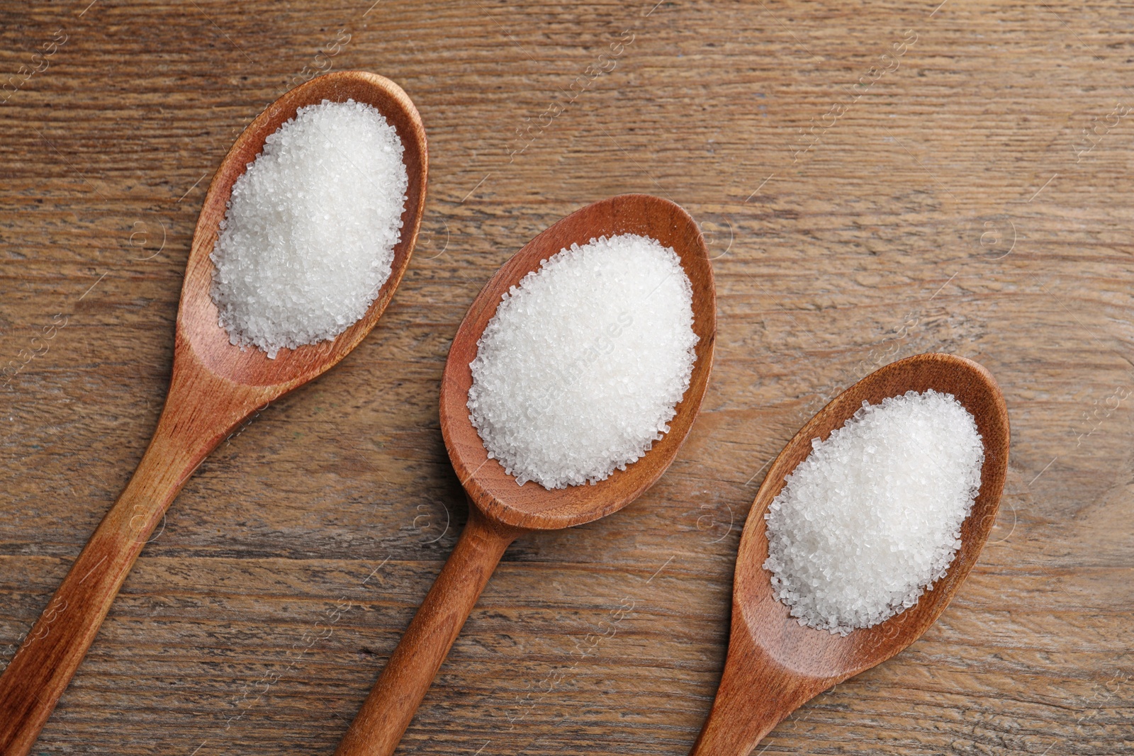 Photo of Granulated sugar in spoons on wooden table, flat lay