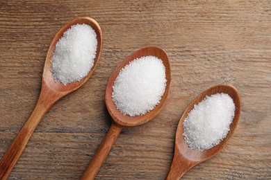 Photo of Granulated sugar in spoons on wooden table, flat lay