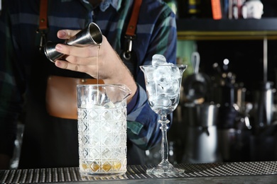 Barman pouring cocktail ingredients into mixing glass at counter in pub, closeup