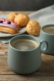 Aromatic coffee in cups, tasty eclairs and profiteroles on wooden table