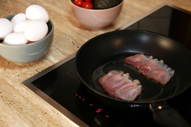 Making tasty breakfast with fried eggs. Cooking bacon in kitchen
