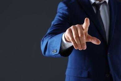 Businessman touching empty virtual screen against dark background, focus on hand