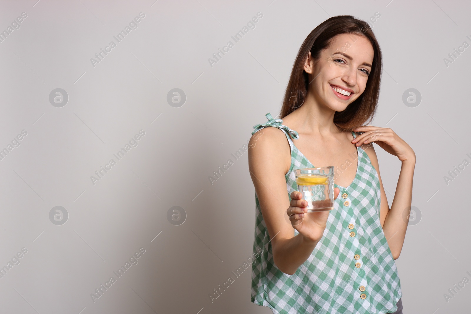 Photo of Young woman with glass of lemon water on light background. Space for text