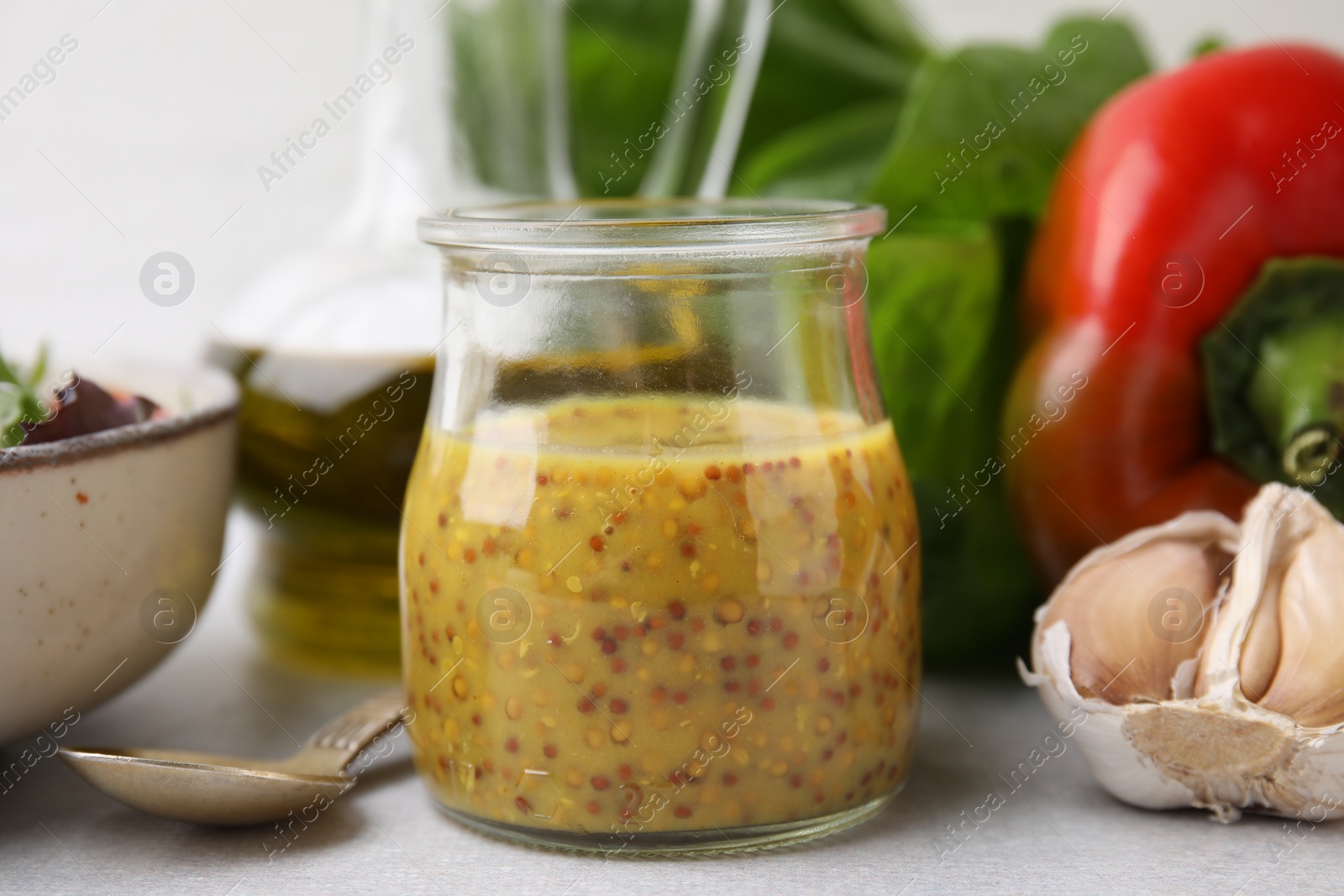 Photo of Tasty vinegar based sauce (Vinaigrette) in jar, garlic and bell pepper on light table, closeup