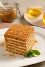 Photo of Slice of delicious layered honey cake with mint on plate, closeup