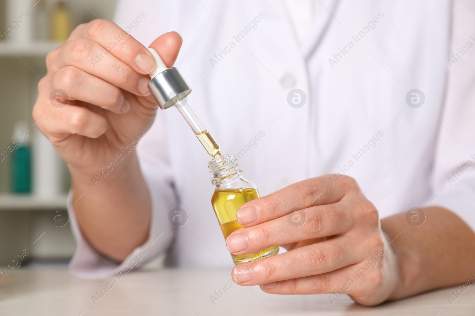 Photo of Dermatologist developing cosmetic oil at white table indoors, closeup