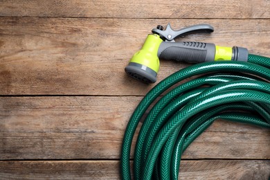 Photo of Green garden hose with spray gun on wooden table, top view. Space for text