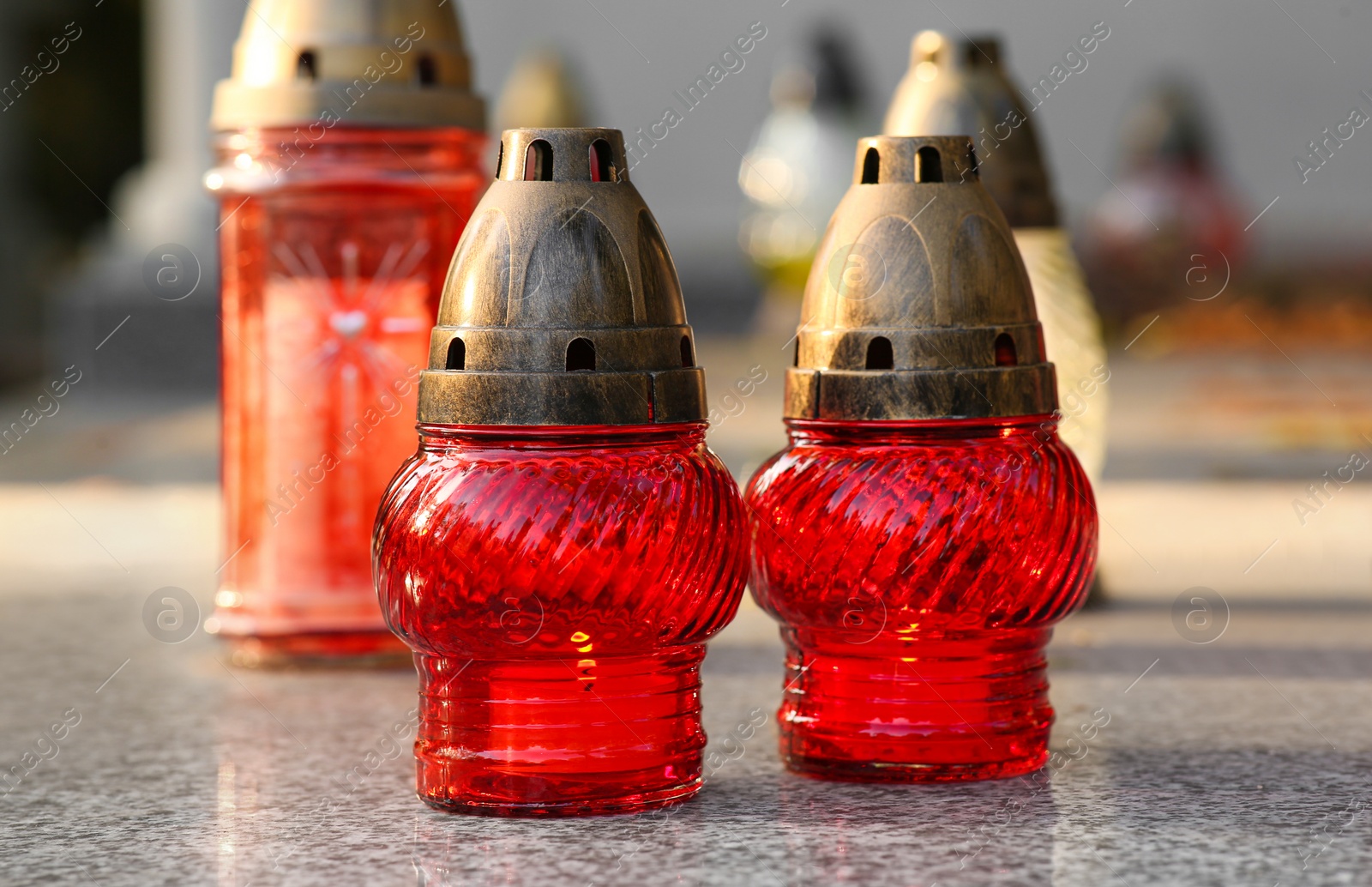 Photo of Different grave lanterns with burning candles on granite tombstone outdoors. Funeral ceremony