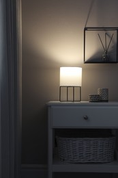 Stylish lamp and candles on white nightstand in room