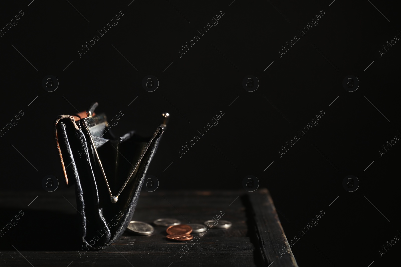 Photo of Wallet and coins on table against dark background with space for text. Poverty concept