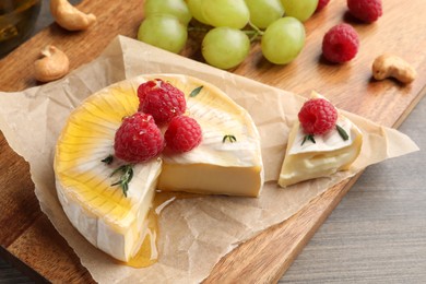 Photo of Brie cheese served with berries and honey on wooden table