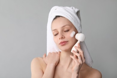 Photo of Young woman washing face with brush and cleansing foam on grey background